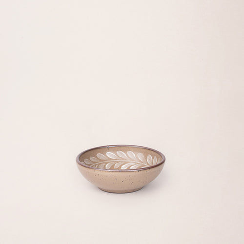 Small ceramic shallow bowl with a hand-painted white leaf border on a pale warm brown interior and exterior with an exposed clay rim.