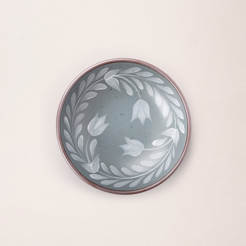 Overhead view of a Medium ceramic shallow bowl with a hand-painted white leaf border on a blue-grey interior and exterior with an exposed clay rim.