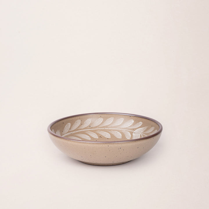 Medium ceramic shallow bowl with a hand-painted white leaf border on a pale warm brown interior and exterior with an exposed clay rim.