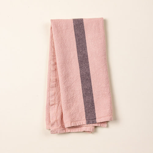 A folded linen towel in a salmon color with a plum stripe in the middle