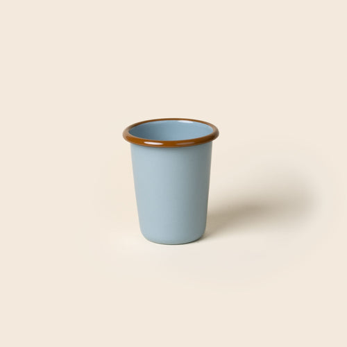 A short robin's egg blue enamel tumbler with a glossy brown rim, set against a soft beige background.