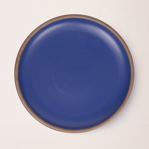 A large ceramic platter in a cobalt blue color featuring iron speckles and an unglazed rim