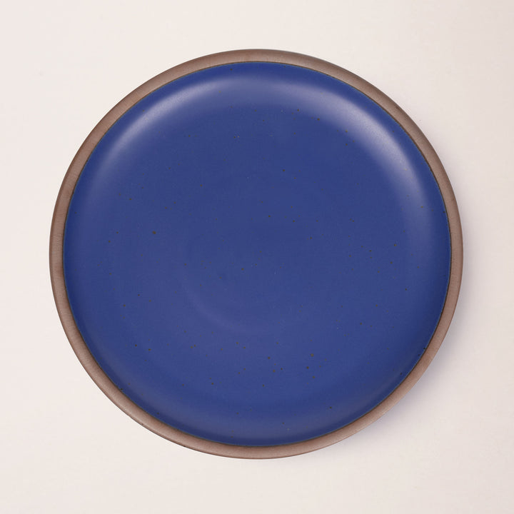 A large ceramic platter in a cobalt blue color featuring iron speckles and an unglazed rim