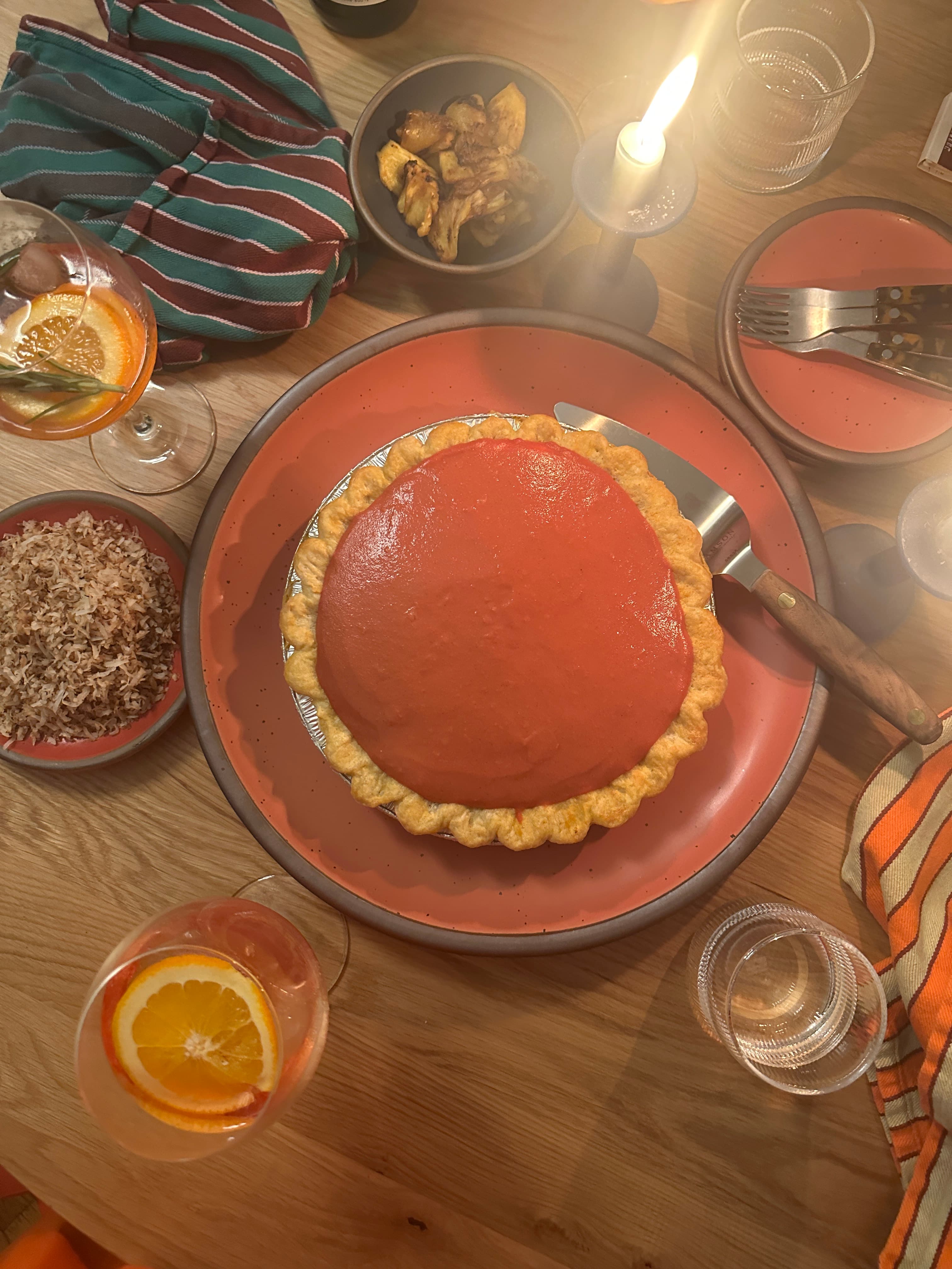 Golden brown pie with smooth guava filling on a coral plate, surrounded by drinks, snacks, and candlelight on a wooden table.