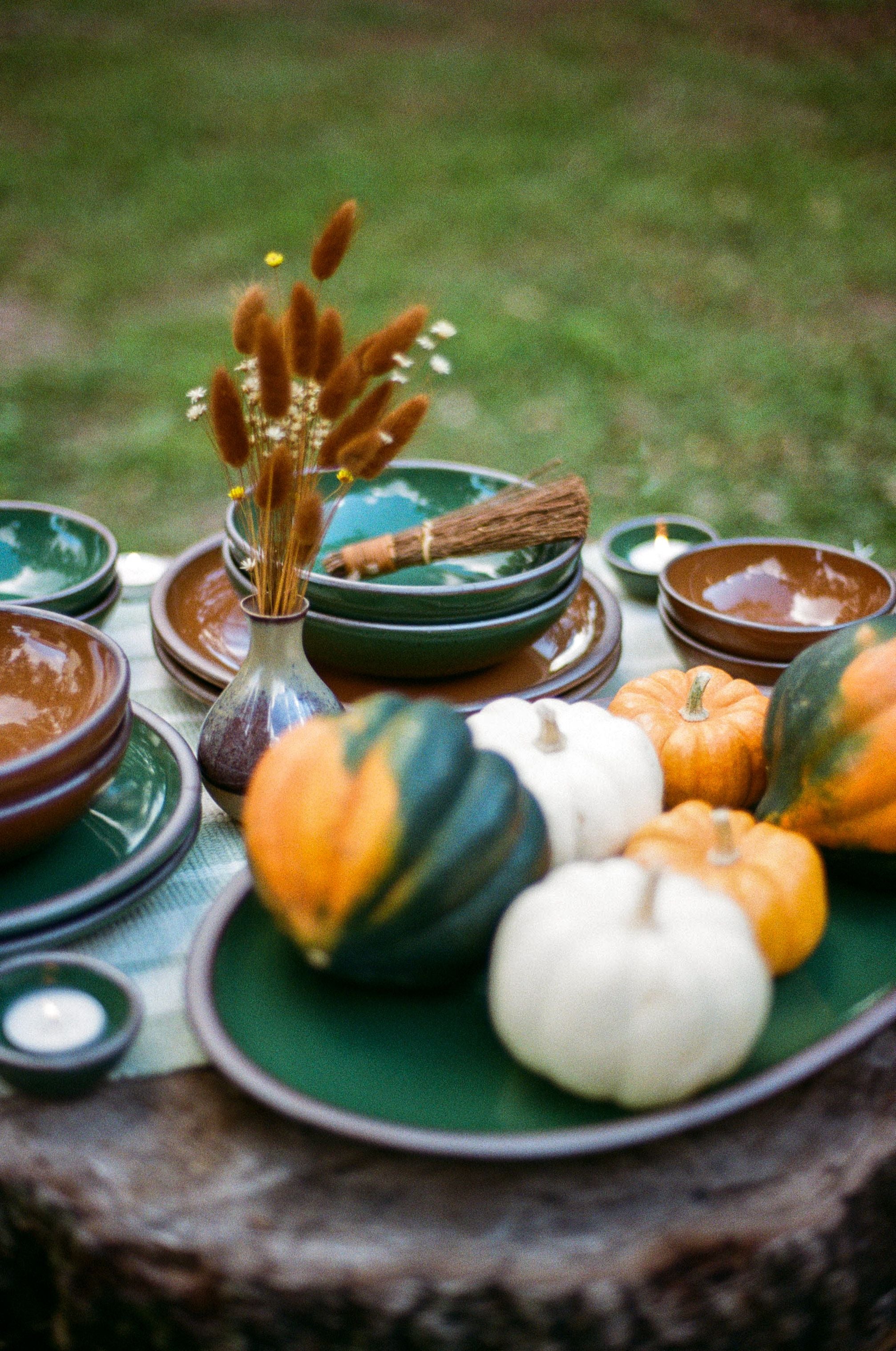 Shiny green and brown pots sit outside on a stump topped with small gourds and dried florals.