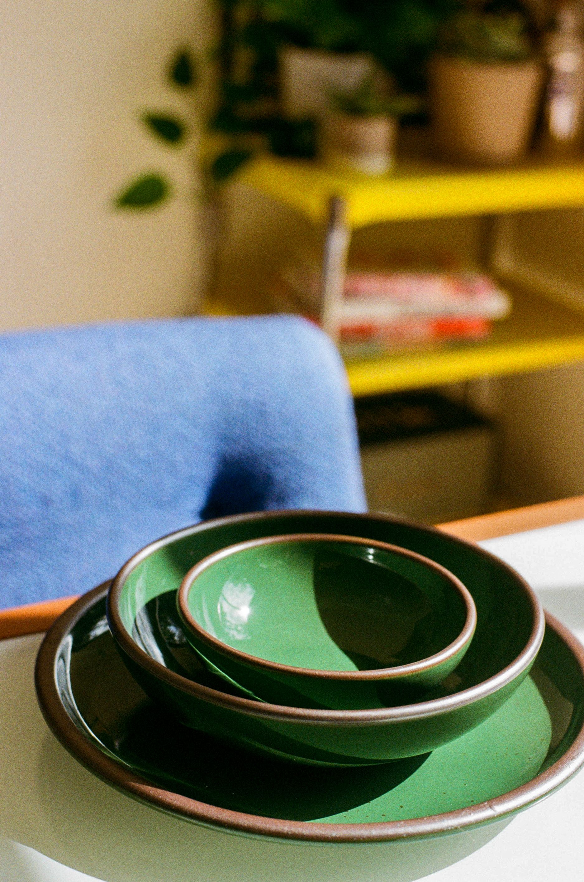 A stack of shiny green pots sit on a dining table with a blue chair and yellow bar cart in the background.