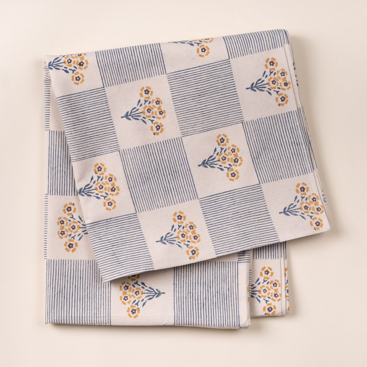 Folded blue-and-white checkered cloth tablecloth printed with small yellow flower bouquets on a light background.