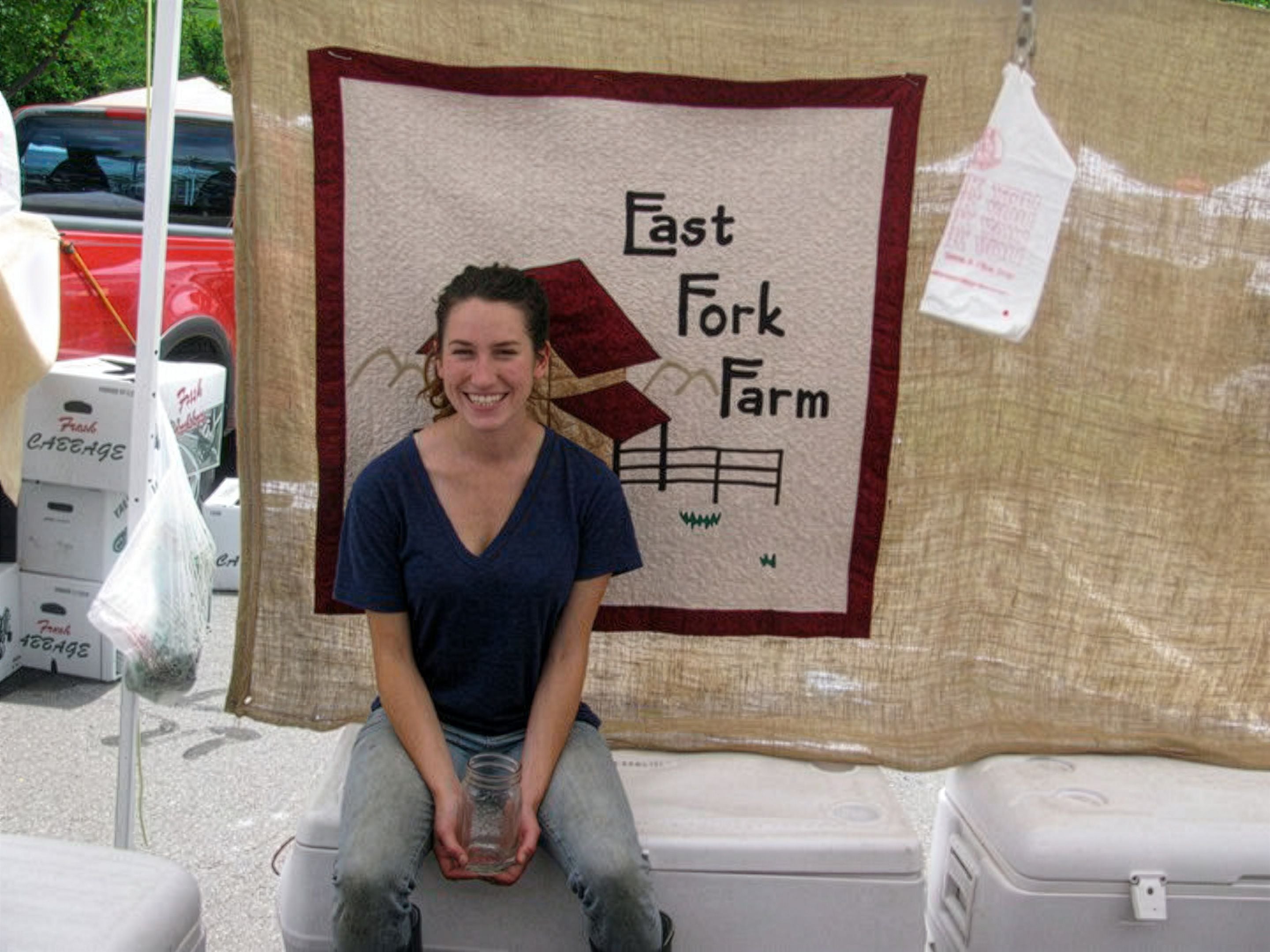 Connie Matisse sitting in front of a sign that reads 'East Fork Farm'