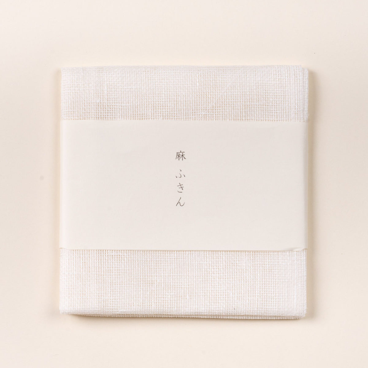 Folded white linen cleaning cloth with a white paper band featuring Japanese text, photographed on a light background.