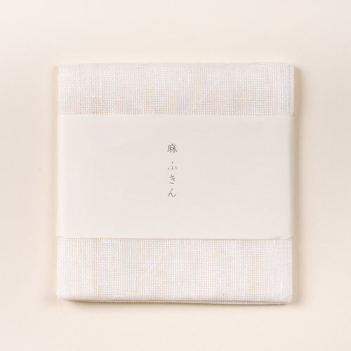 Folded white linen cleaning cloth with a white paper band featuring Japanese text, photographed on a light background.