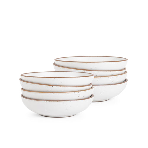 A stack of 8 dinner-sized shallow ceramic bowls in a cool white color featuring iron speckles and an unglazed rim