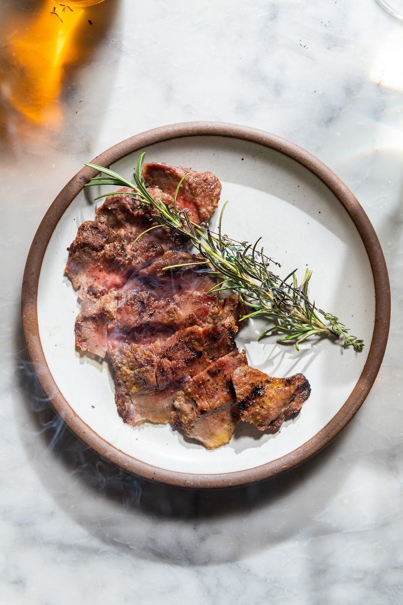 Thin sliced steak plated on East Fork Eggshell plate with rosemary and smoke 