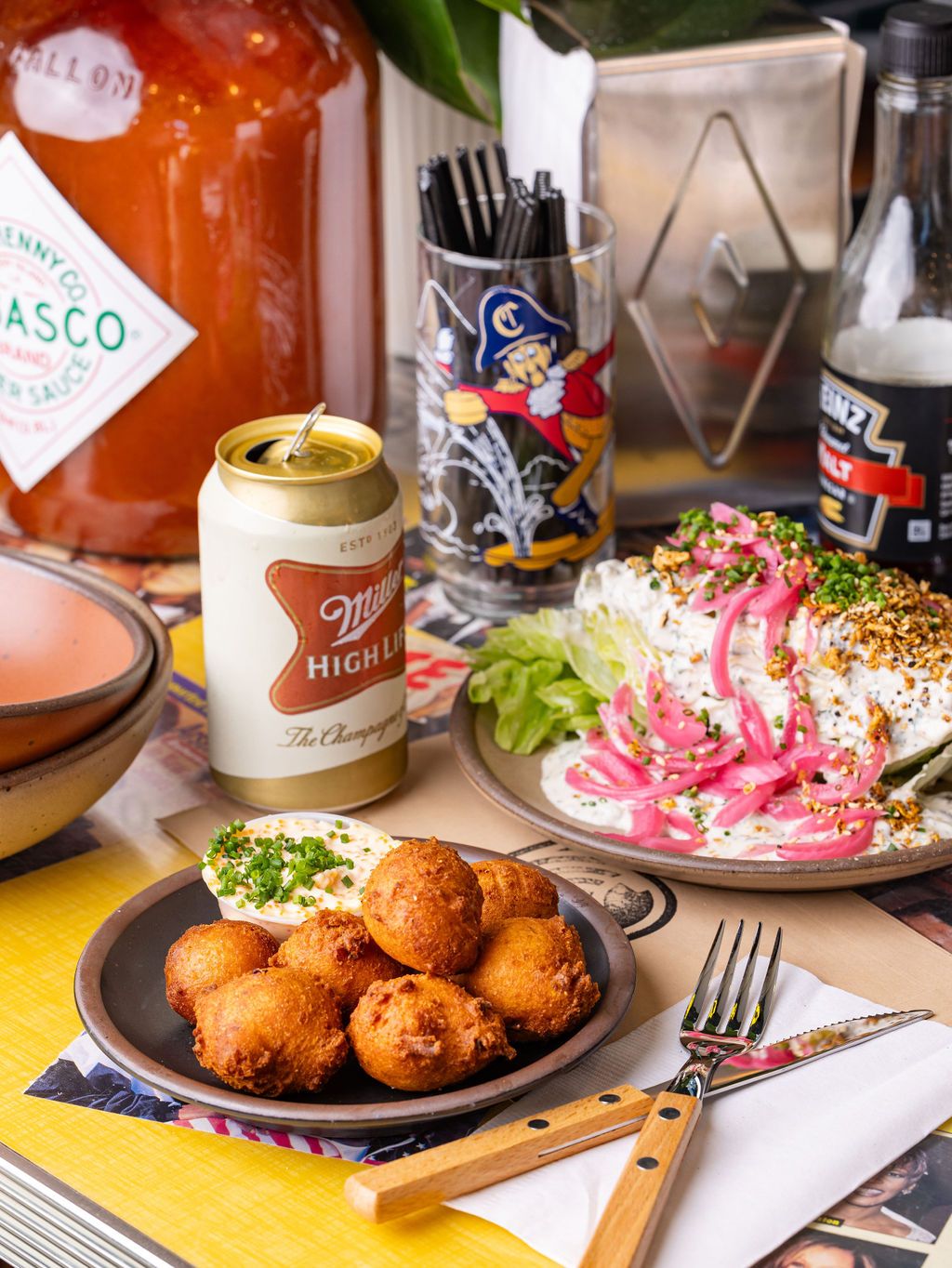 A few ceramic plates of food with hushpuppies and vegetables, a beer, and utensils