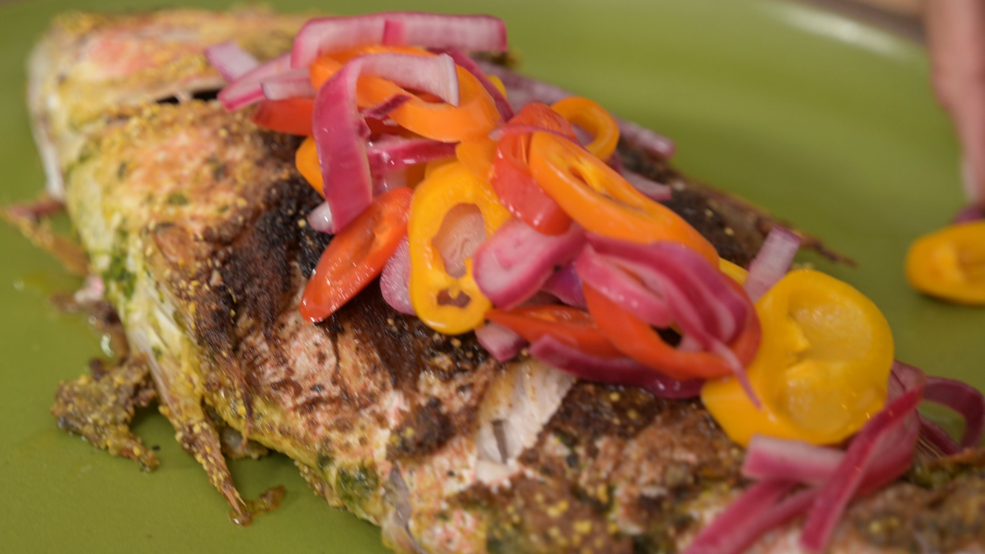 Colorful peppers and onions on a fish sitting on a green ceramic plate.