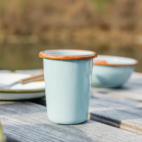 Light blue enamel tumbler with a brown rim sitting on a weathered wooden deck outdoors.
