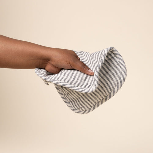Hand holds out a square quilted linen potholder in black and white stripes with rounded corners and a small ‘LINEN TALES’ label, against a light background.