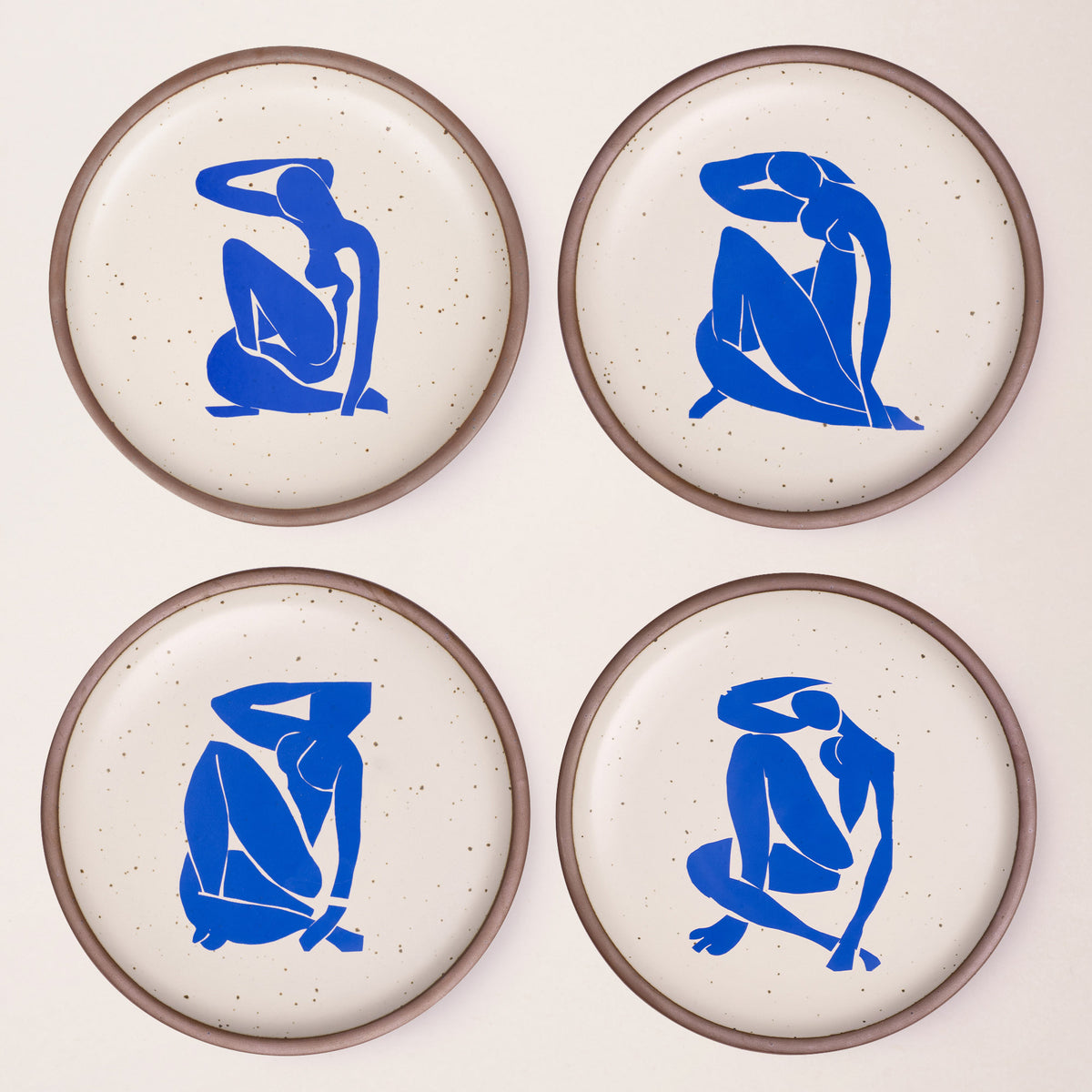 Four ceramic dinner plates in warm off-white colors and unglazed rim, each with a different blue decal from the Nu Bleu series by Henri Matisse.