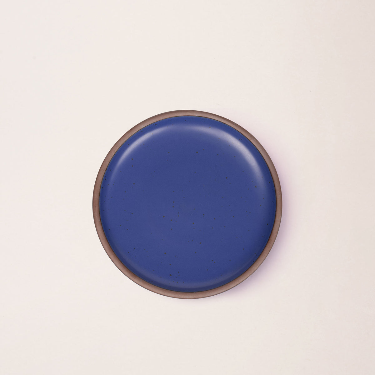 A medium sized ceramic plate in a cobalt blue color featuring iron speckles and an unglazed rim.