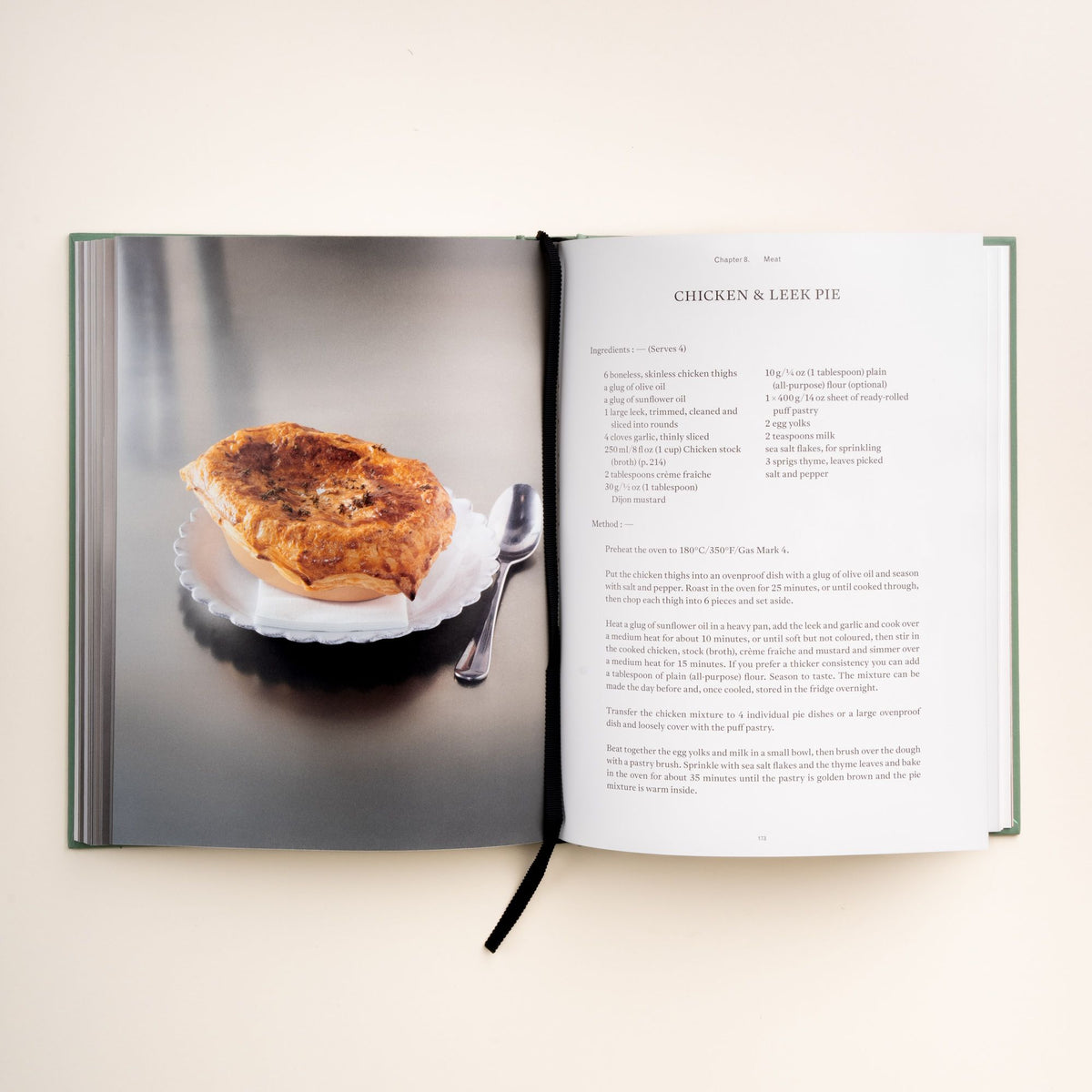 Open cookbook displaying a recipe for Chicken & Leek Pie, with a photo of the golden pie on a white scalloped plate beside a spoon.
