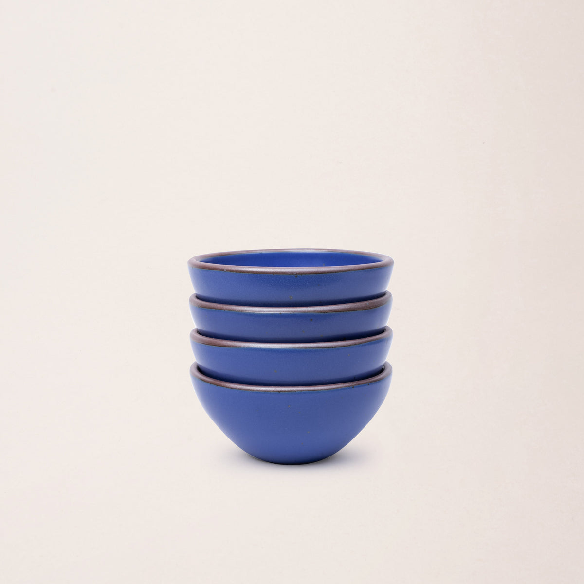 A stack of 4 small dessert sized rounded ceramic bowls in a cobalt blue color featuring iron speckles and an unglazed rim