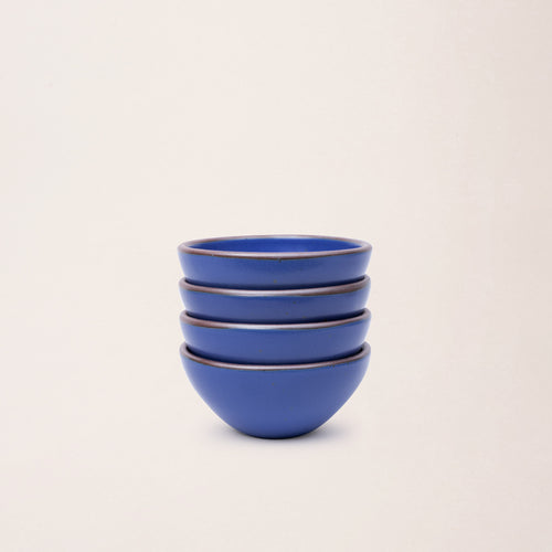 A stack of 4 small dessert sized rounded ceramic bowls in a cobalt blue color featuring iron speckles and an unglazed rim
