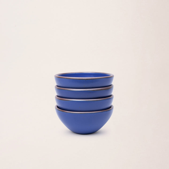 A stack of 4 small dessert sized rounded ceramic bowls in a cobalt blue color featuring iron speckles and an unglazed rim
