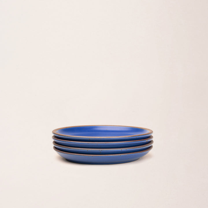 4 medium sized ceramic plates in a cobalt blue color featuring iron speckles and an unglazed rim.