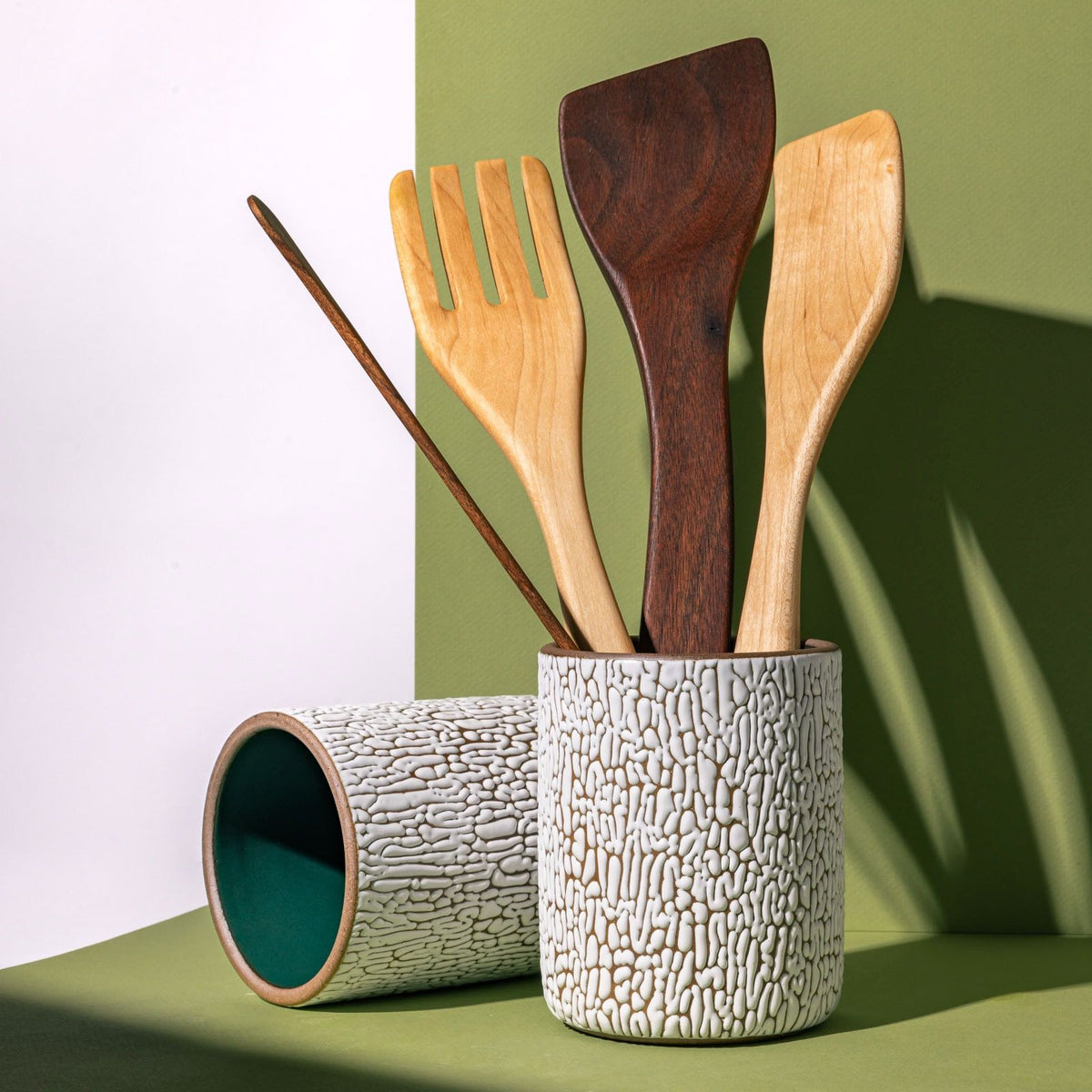 Two big white ceramic vessel with cracks and the interior being dark teal filled with wooden utensils