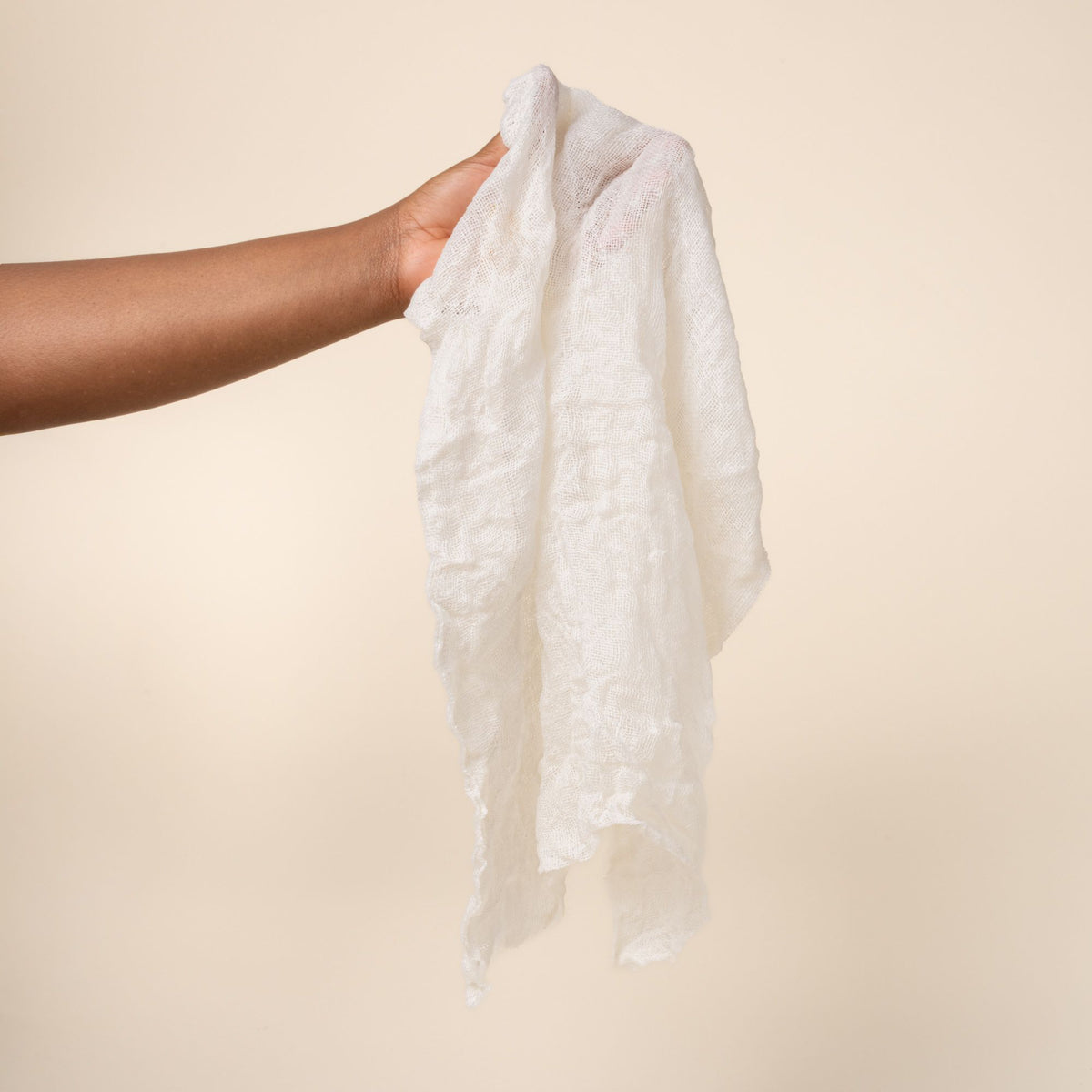 Hand holding a loose and wet natural linen cleaning cloth showing a subtle woven texture and stitched edges.