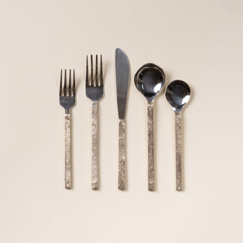 Five-piece stainless steel and brass flatware set with two forks, a knife, and two spoons on a light background