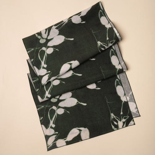 Dark green linen table runner with white botanical print, folded neatly on a neutral background.