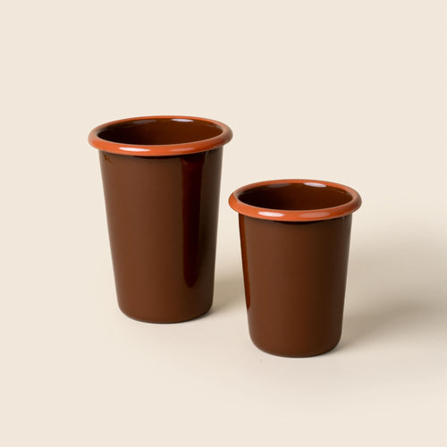 A small and tall red-brown enamel tumblers with an orange rim, set against a soft beige background.