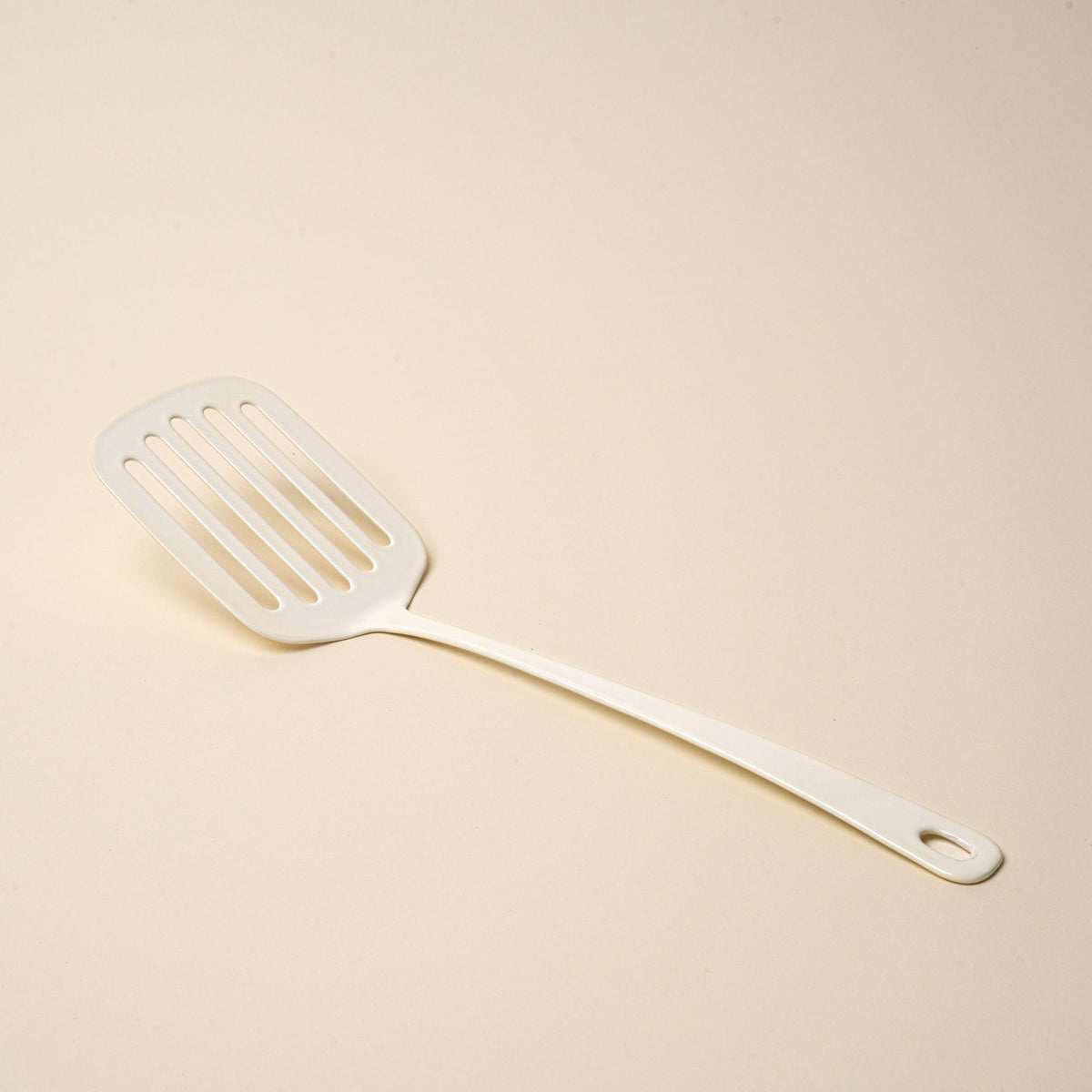 A white enamel spatula with a hole at the end of the handle for hanging.