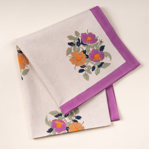 Folded cream linen towel with a purple border and floral print in purple and orange on a light background.