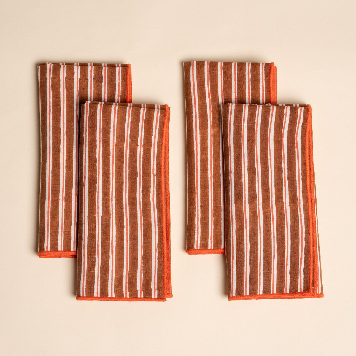 A set of four folded cloth napkins with vertical brown and white stripes, finished with bright orange edging.