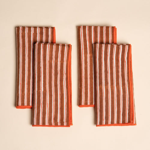 A set of four folded cloth napkins with vertical brown and white stripes, finished with bright orange edging.