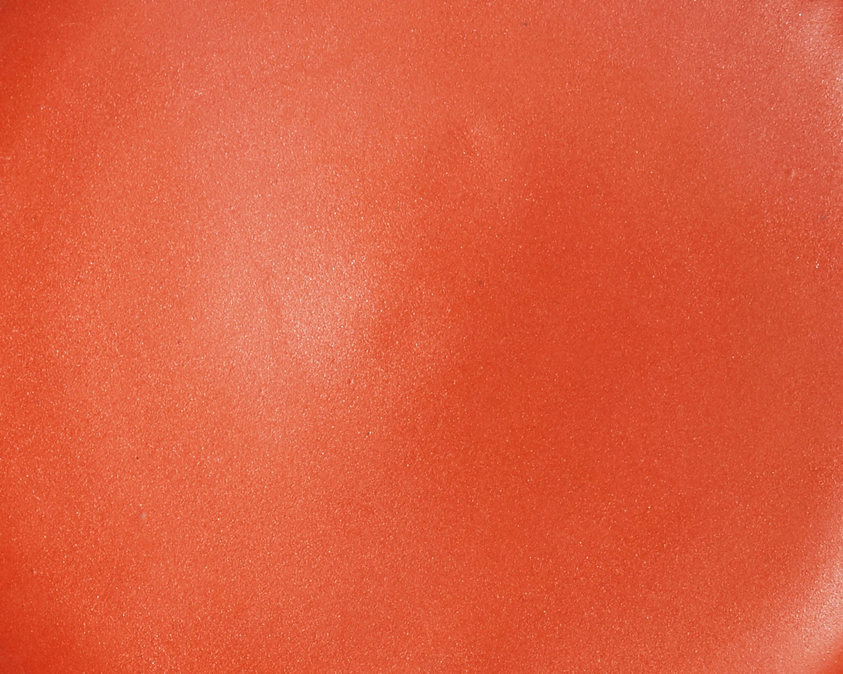 A closeup of a ceramic plate in a fiery orange color with a few subtle iron speckles throughout