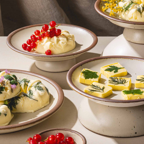 Small ceramic dessert-sized cake plate with beautiful butter sculptures on top with fruit and herbs.