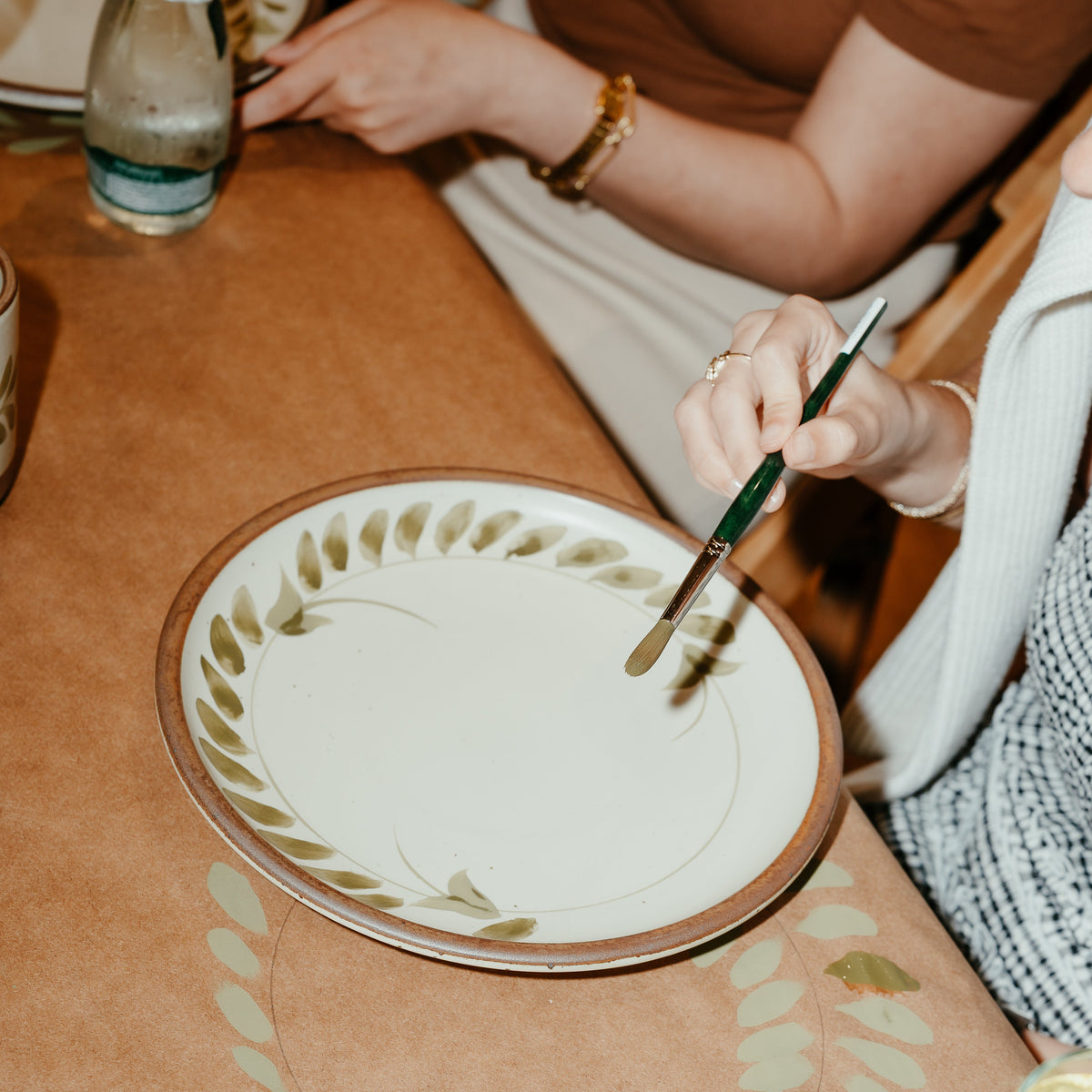 A hand holding a paintbrush painting a plate in a workshop.
