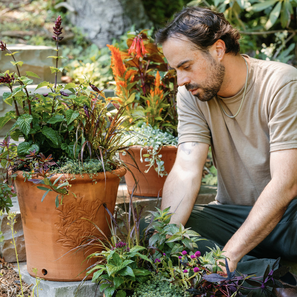 Alex in the garden tending to plants in large terracotta pots with botanical designs on them.