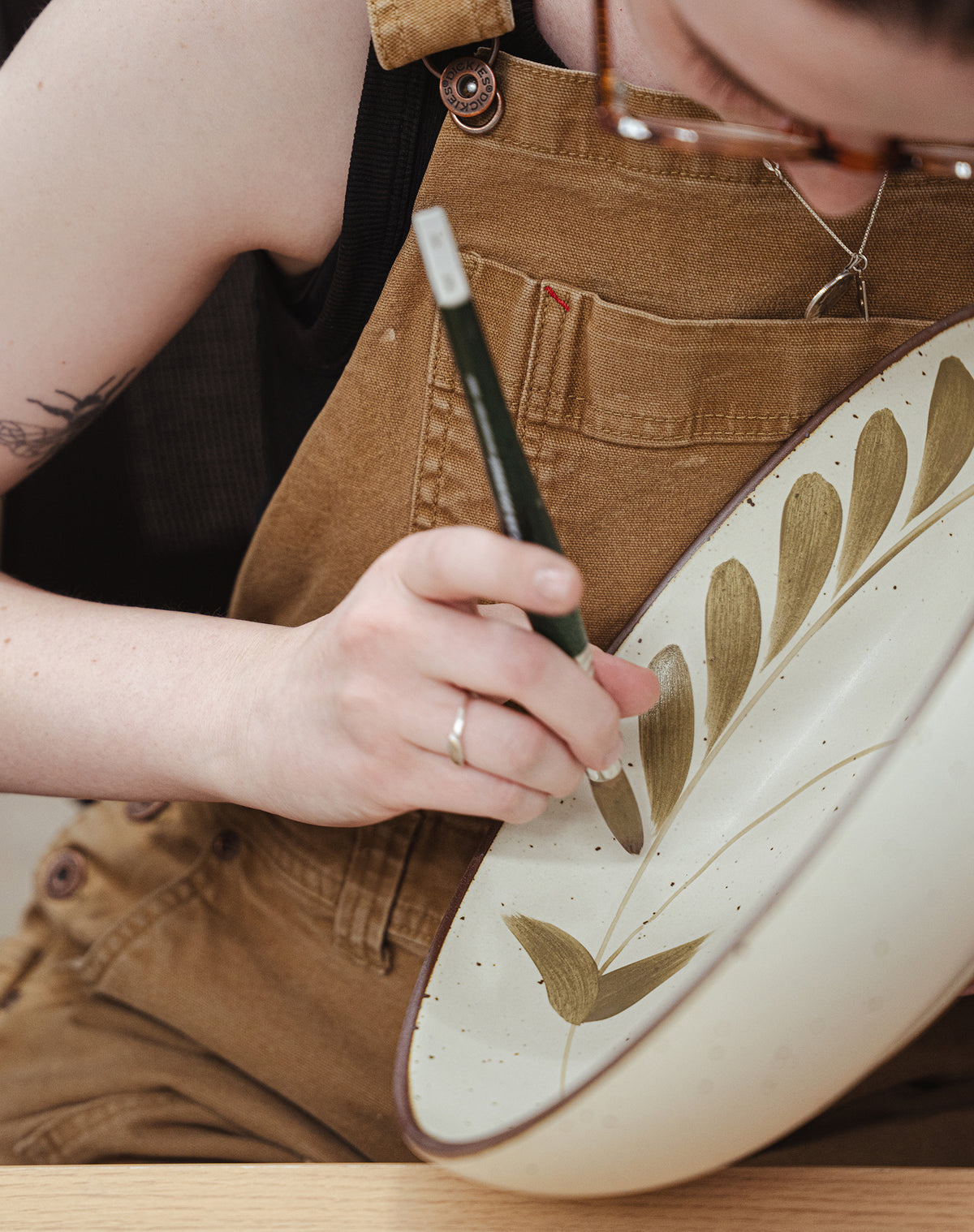 Hand painting an olive greenery and tulip motif on a cream ceramic plate.