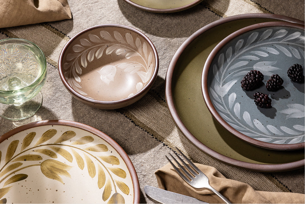 An overhead view of a table with hand painted dinnerware, silverware, napkin, and a coupe glass.