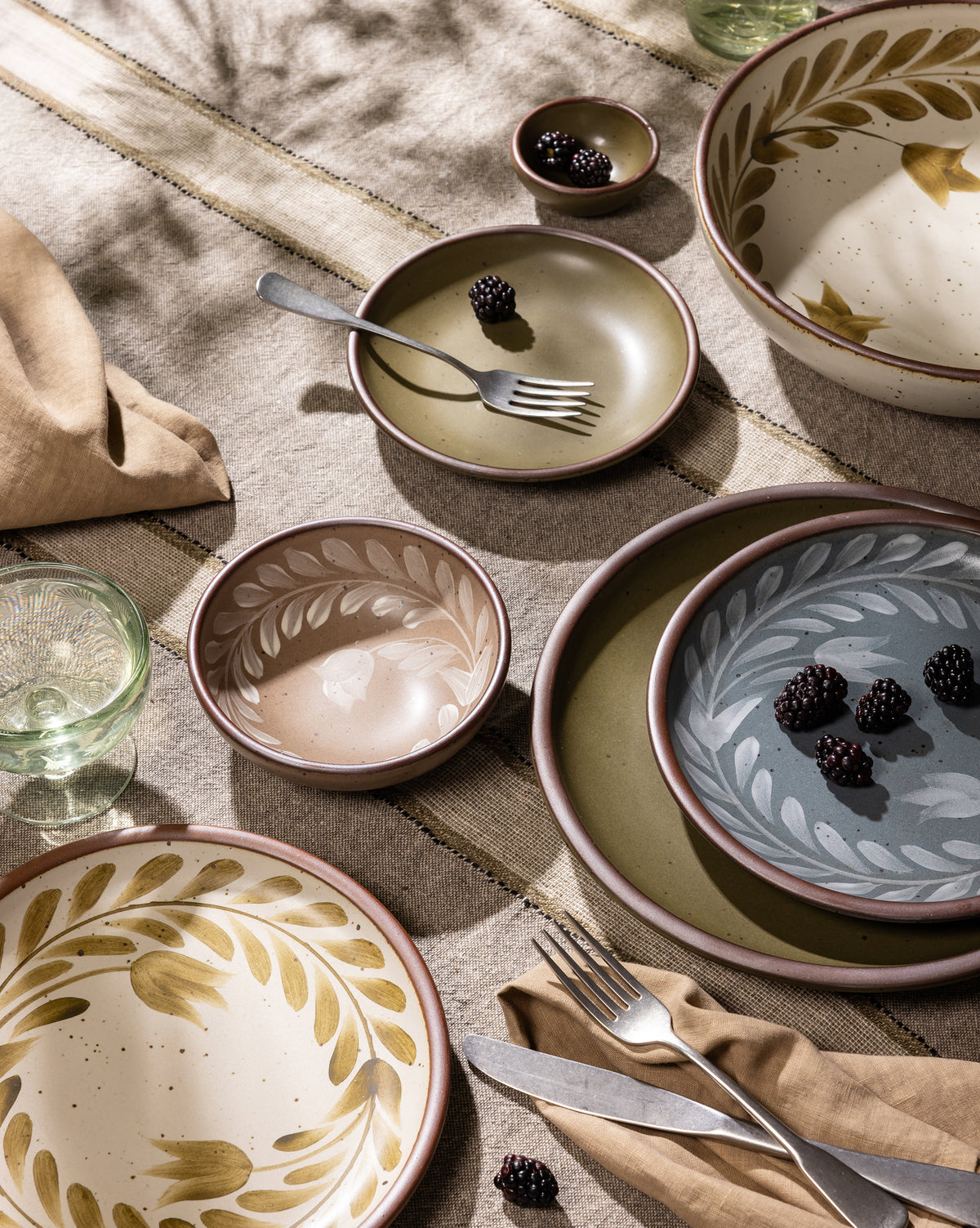 An overhead view of a table with hand painted dinnerware, silverware, napkin, and a coupe glass.