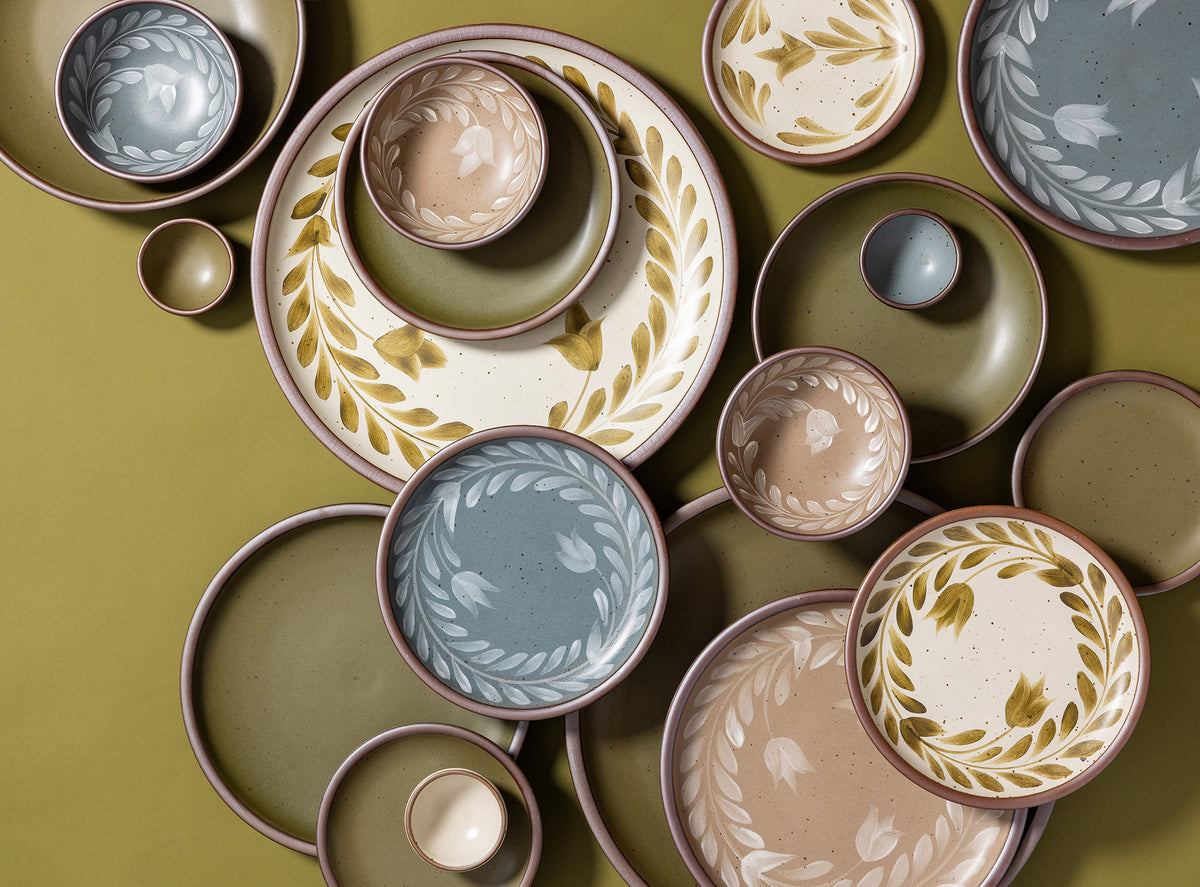 An overhead view of hand painted ceramic dinnerware featuring a tulip crown design against a green background.