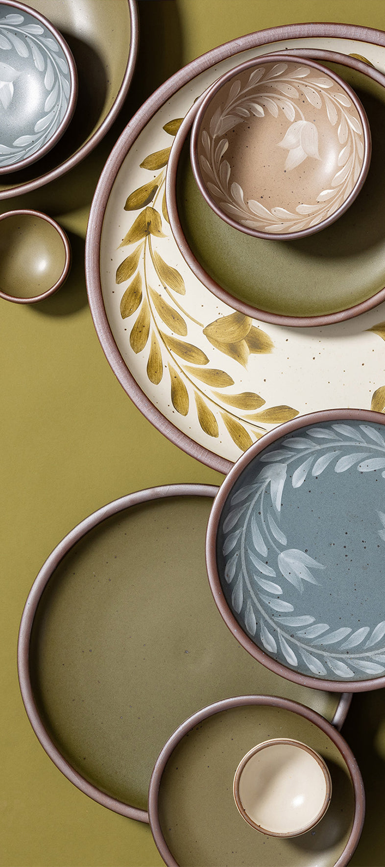 An overhead view of hand painted ceramic dinnerware featuring a tulip crown design against a green background.