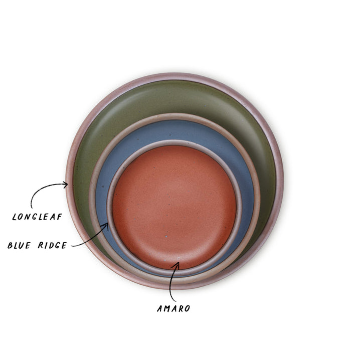 Three nested ceramic plates with different colors, olive green, blue, and and cool terracotta with labels on a white background