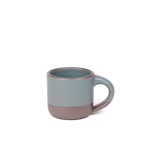 A small sized ceramic mug with handle in a blue-grey glaze featuring iron speckles and unglazed rim and bottom base.