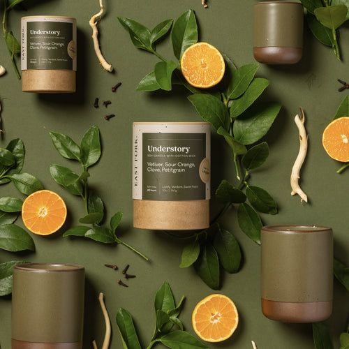 An overhead view of a olive green ceramic candle artfully arranged with orange, petitgrain and clove.