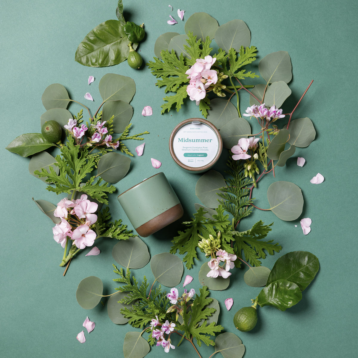 An overhead view of a green ceramic candle artfully arranged with bergamot, eucalyptus, rose geranium and cypress.
