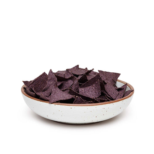 A large shallow serving ceramic bowl in a cool white color featuring iron speckles and an unglazed rim, filled with tortilla chips